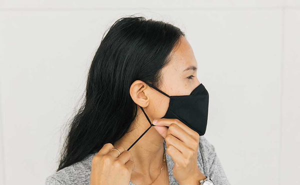 Person tightening/adjusting the ear loops on the V6 Mask, Black, size Small/Medium.